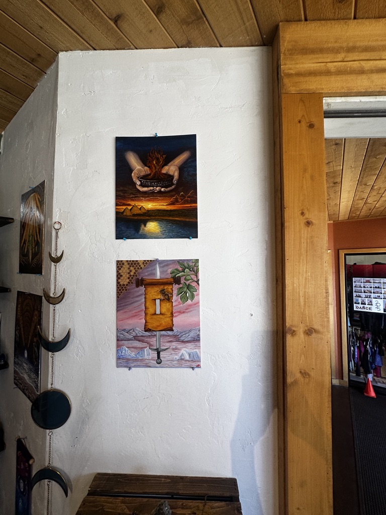 Two original paintings hanging on a white plaster wall in the shop