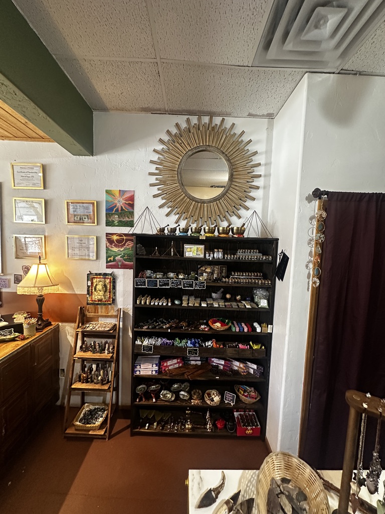 A tall shelf of incense, oils, singing bowls, and small carvings under a sunburst mirror